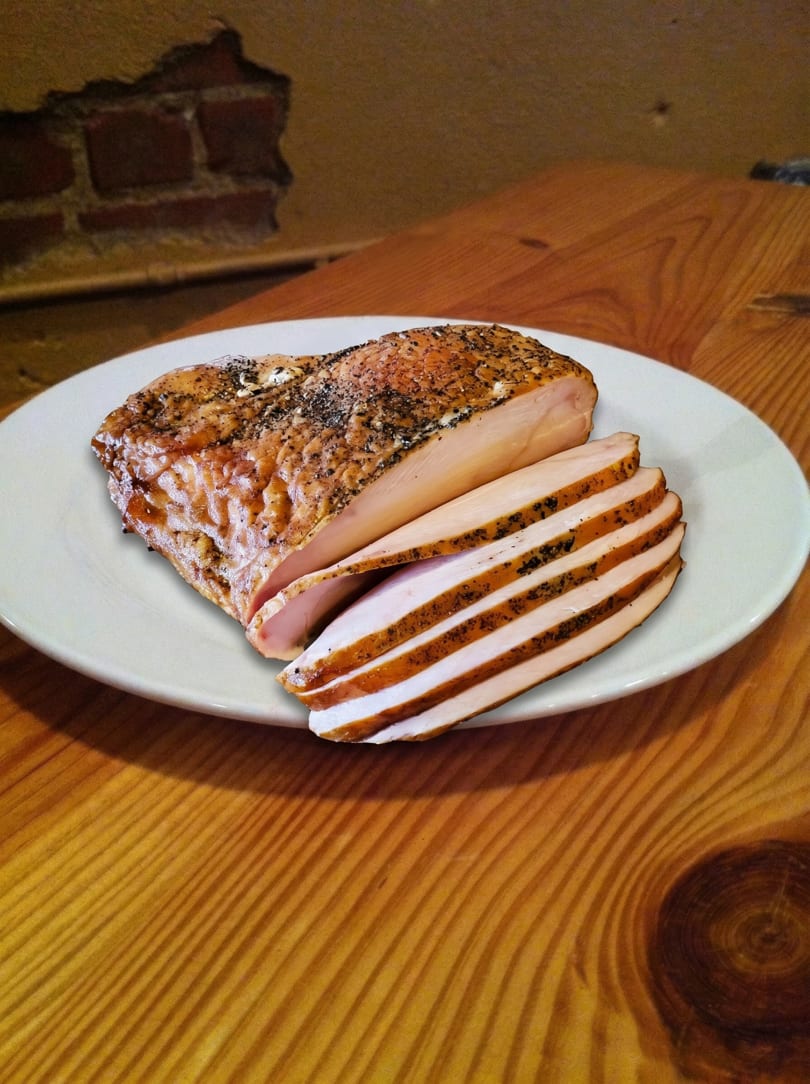 Seasoned, sliced smoked chicken breast on a white plate, resting on a rustic wooden table.