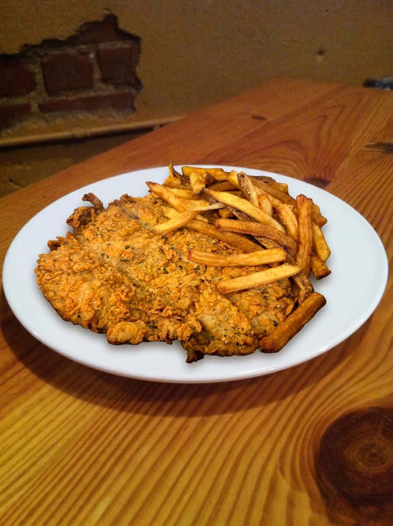 Crispy fried chicken cutlet and golden french fries on a white plate, on a wooden table.