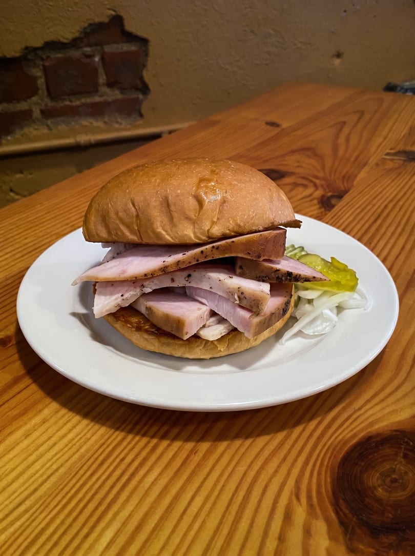 A turkey sandwich with pickles and onions on a white plate, on a wooden table.