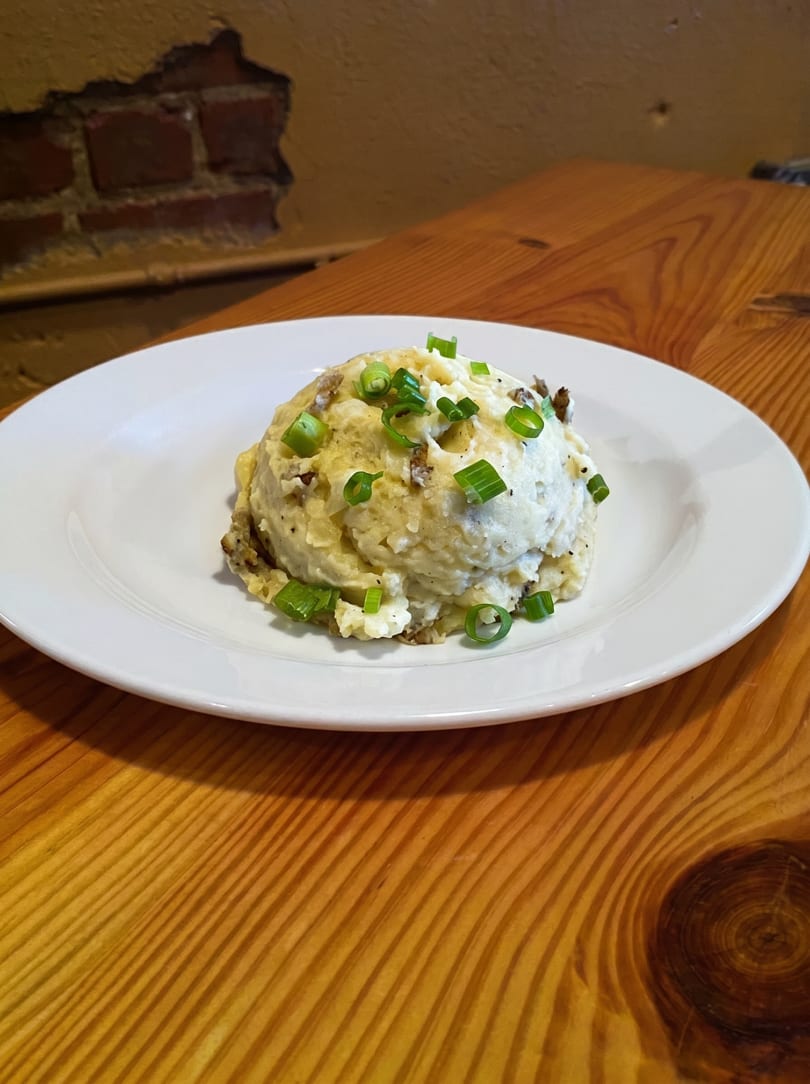 A serving of mashed potatoes topped with chopped green onions on a white plate.