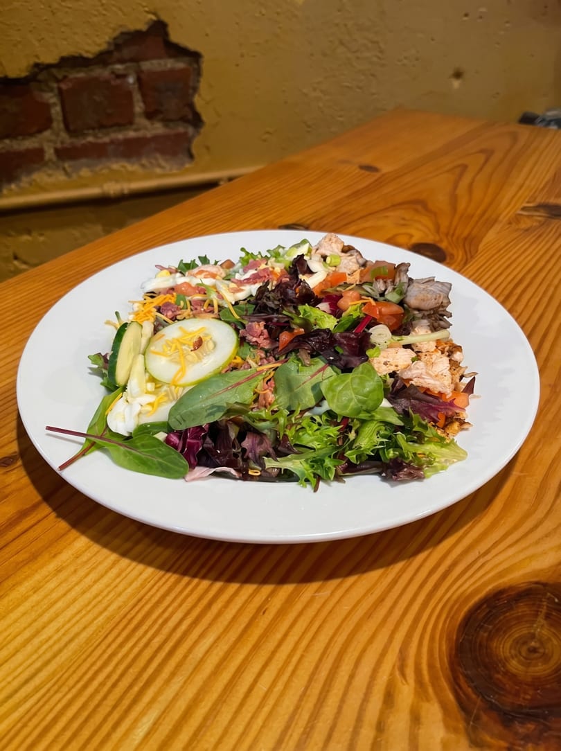 A vibrant salad with mixed greens, chicken, bacon, cheese, and cucumbers on a white plate.