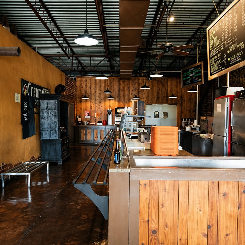 Rustic restaurant interior with wooden walls, industrial lighting, a long counter, and kitchen equipment.